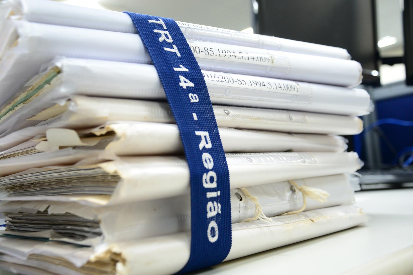 processos físicos empilhados amarrados com uma fita elástica com a inscrição TRT 14ª Região