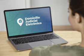 Uma pessoa em frente ao notebook sobre a mesa, com o texto na tela: Domicílio Judicial Eletrônico